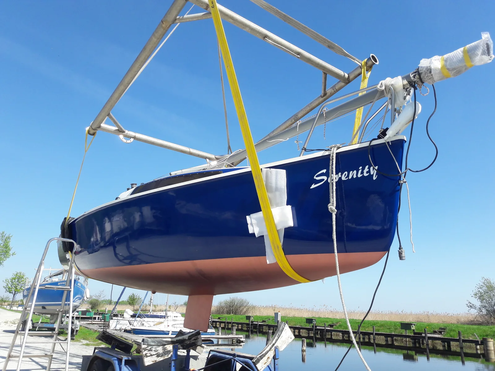 Blaue Segelyacht in gelben Hebegurten beim Kranen am Hafen